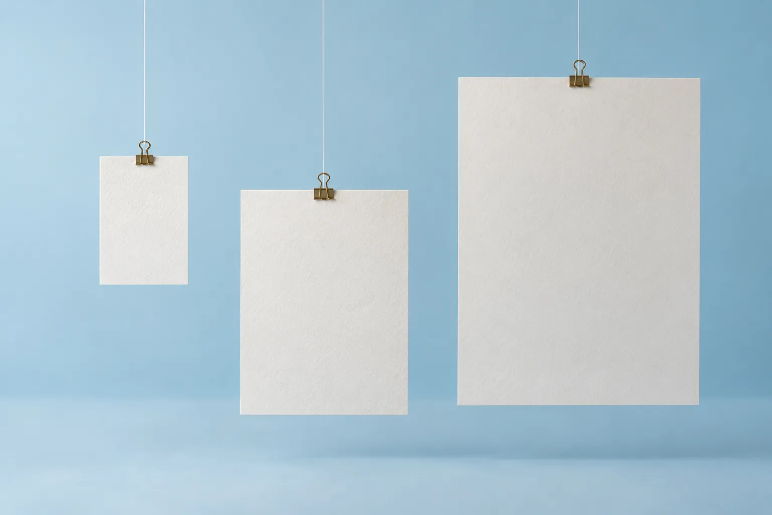 Three differently sized paper rectangles suspended in a pale-blue studio