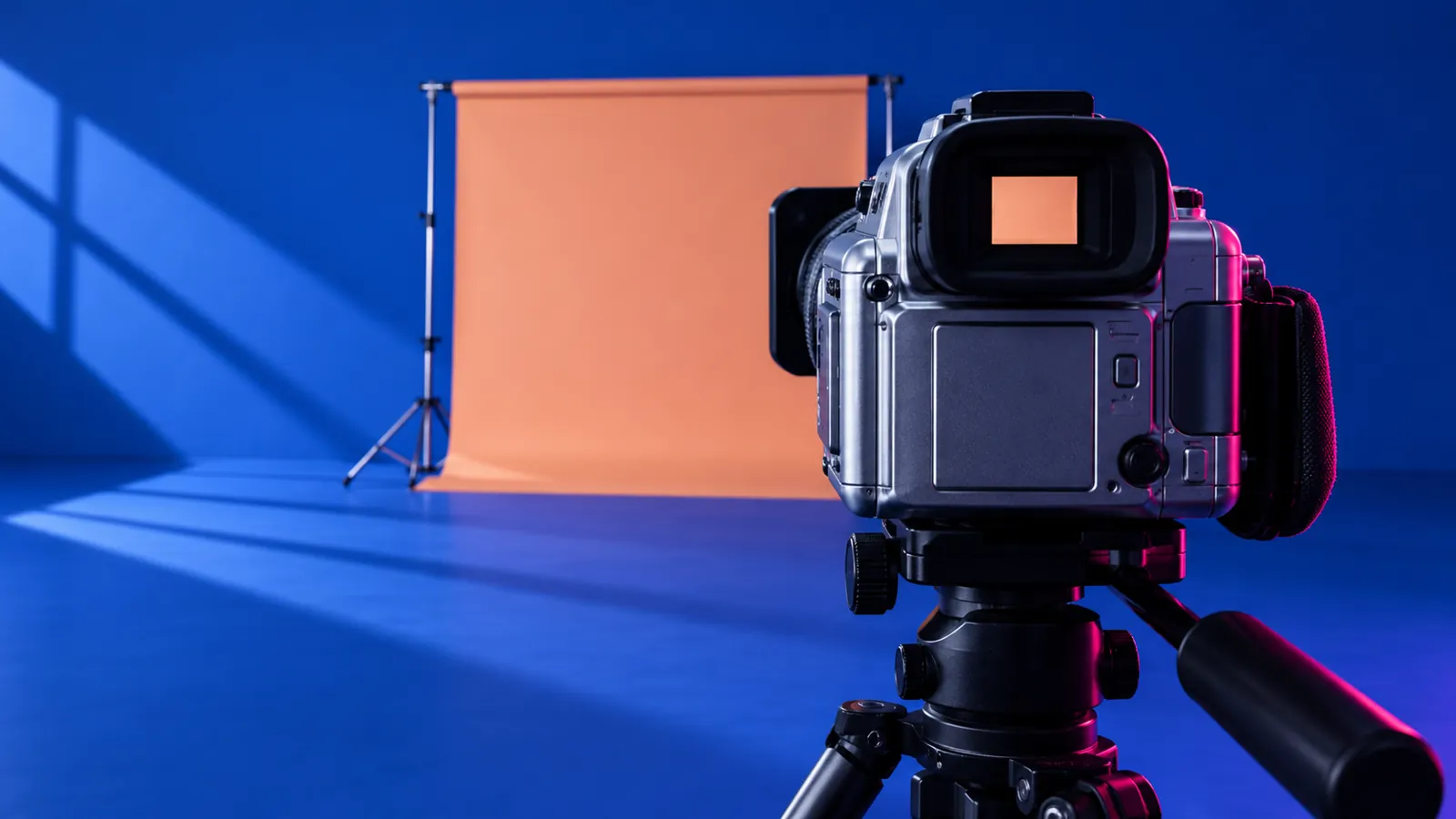 Conceptual camera on a tripod in a cobalt studio facing a peach backdrop